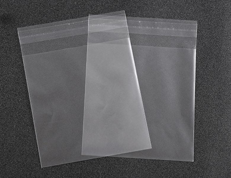 Three clear, empty plastic bags with adhesive strips at the top, arranged in a fan shape on a dark background.