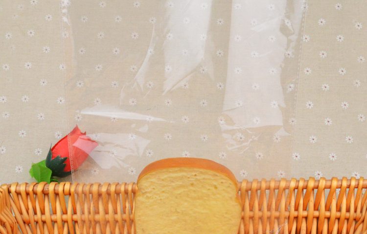 A clear plastic bag containing a single slice of bread, placed in a wicker basket with a small artificial rose.