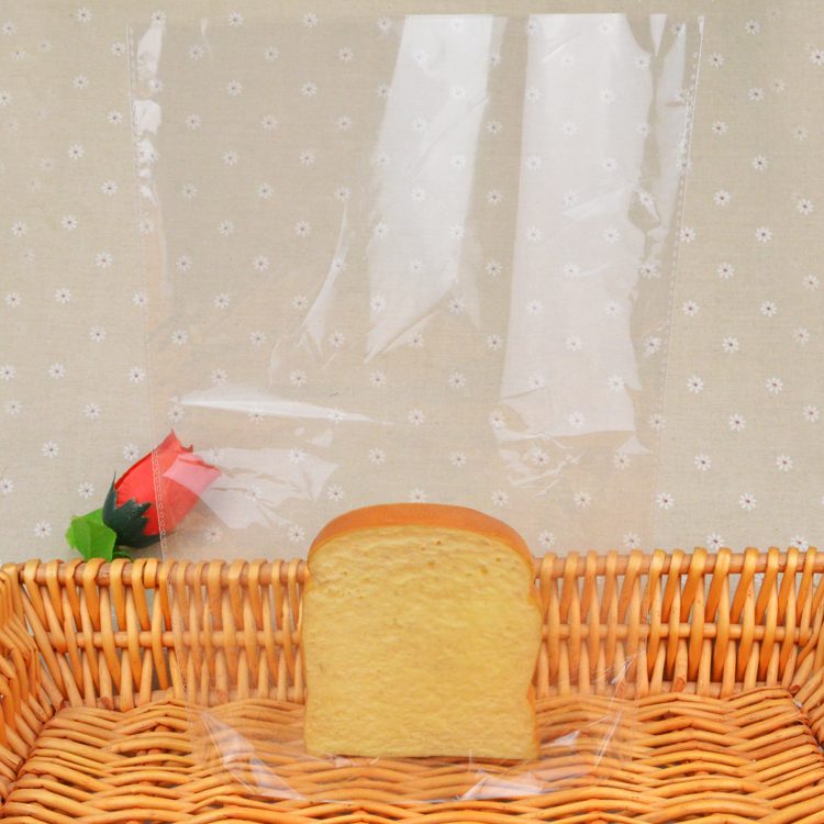 A clear plastic bag containing a single slice of bread, placed in a wicker basket with a small artificial rose.