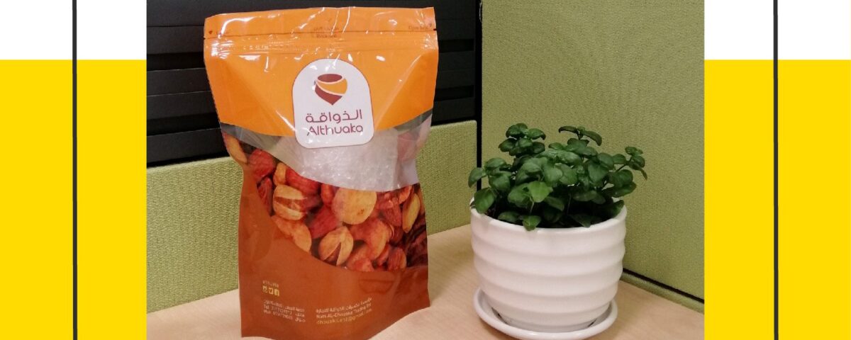 A stand-up pouch with a clear window containing dried fruit sits next to a small green plant in a white pot on a desk.