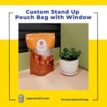A stand-up pouch with a clear window containing dried fruit sits next to a small green plant in a white pot on a desk.