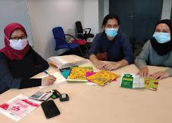 Three people wearing face masks sitting at a table with documents and office supplies.