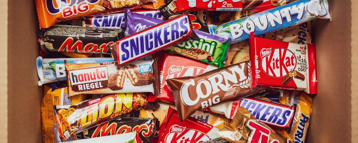 A top-down view of a cardboard box packed with various branded chocolate and cereal bars.