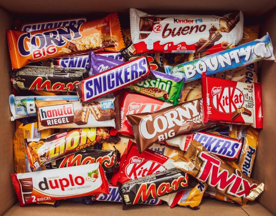 A top-down view of a cardboard box packed with various branded chocolate and cereal bars.