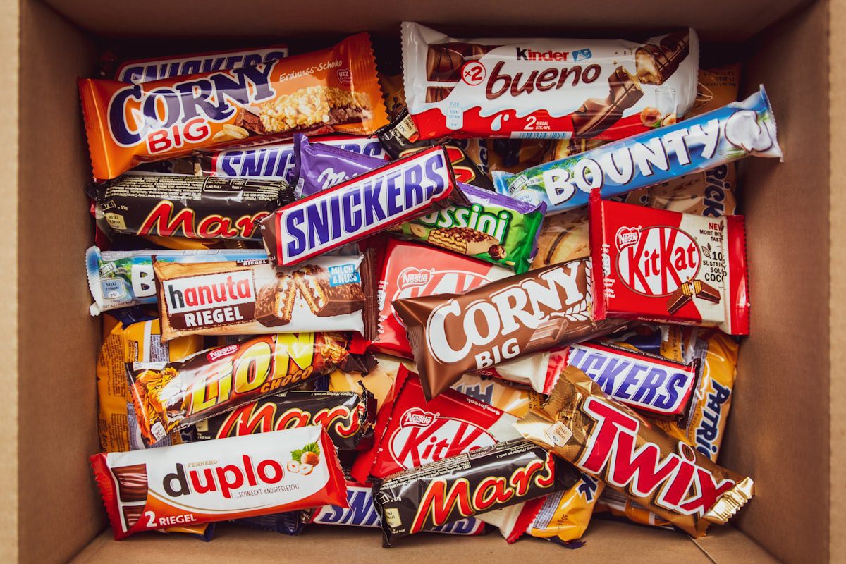 A top-down view of a cardboard box packed with various branded chocolate and cereal bars.